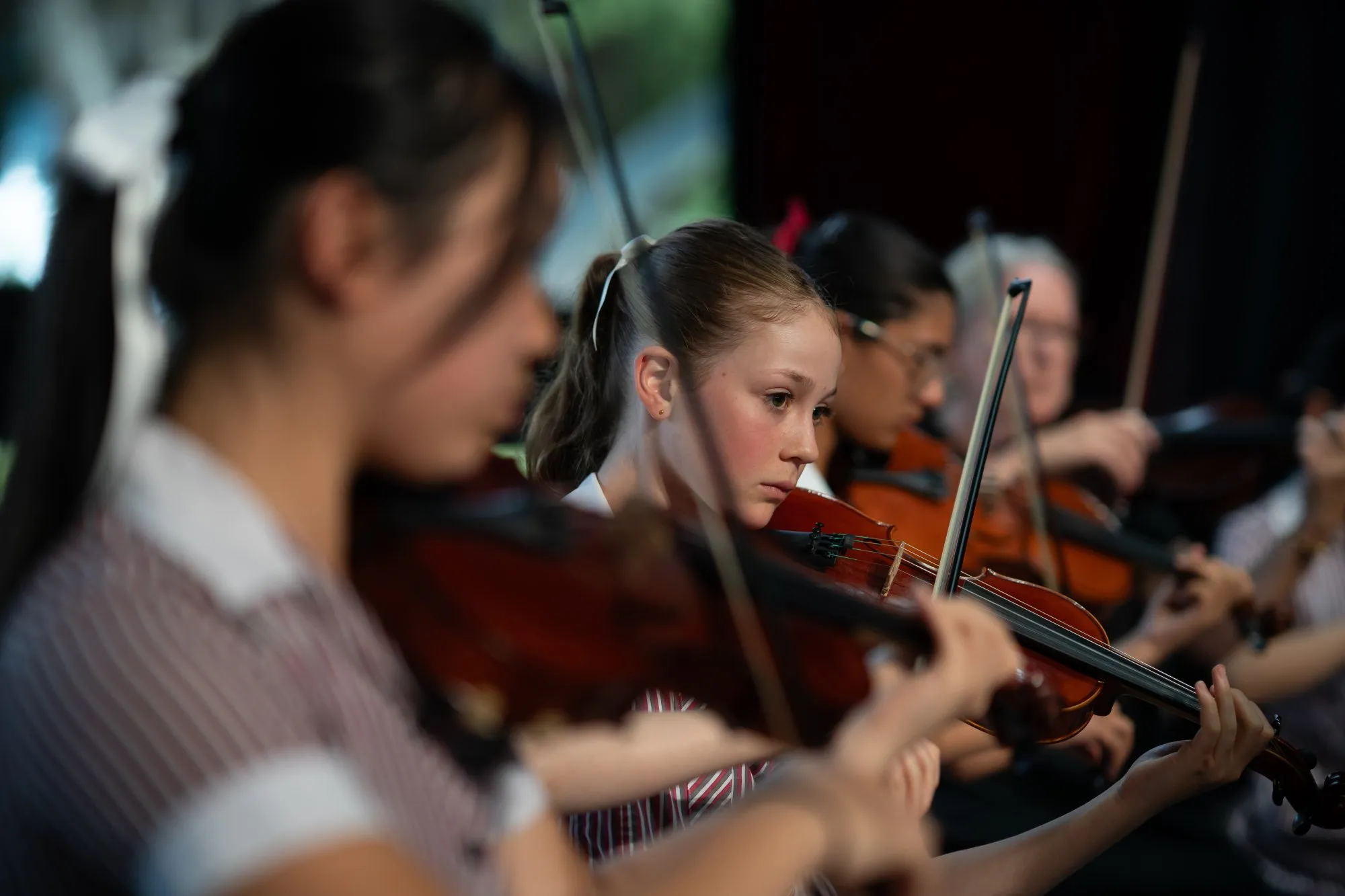 Focused young female violinists playing in an orchestra, with one girl prominently in the center.