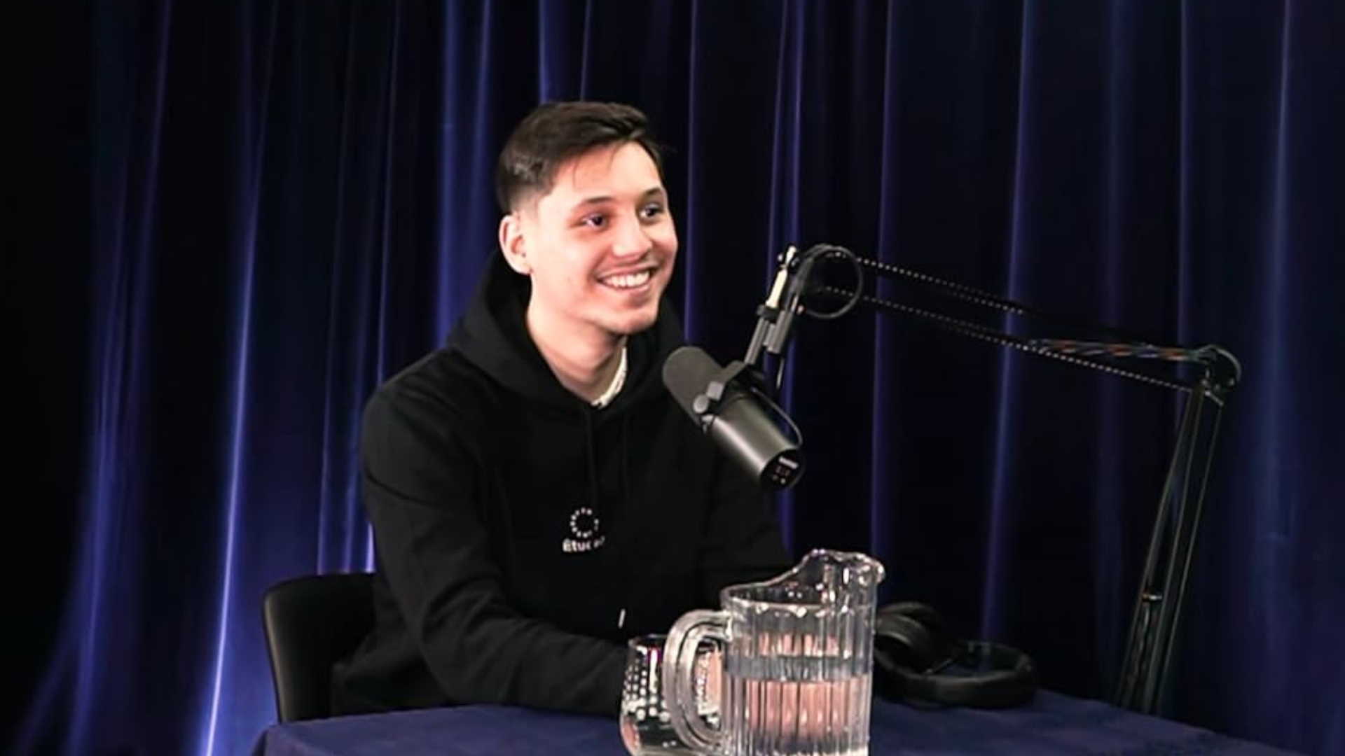 Alex The Lucky, real name Alexis Lachance, smiling at a podcast microphone