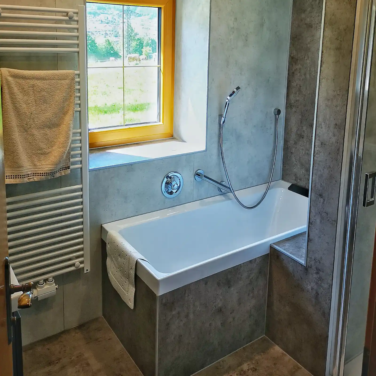 Modernes Badezimmer mit Badewanne, großformatigen Fliesen in Betonoptik und klarer Architektur.