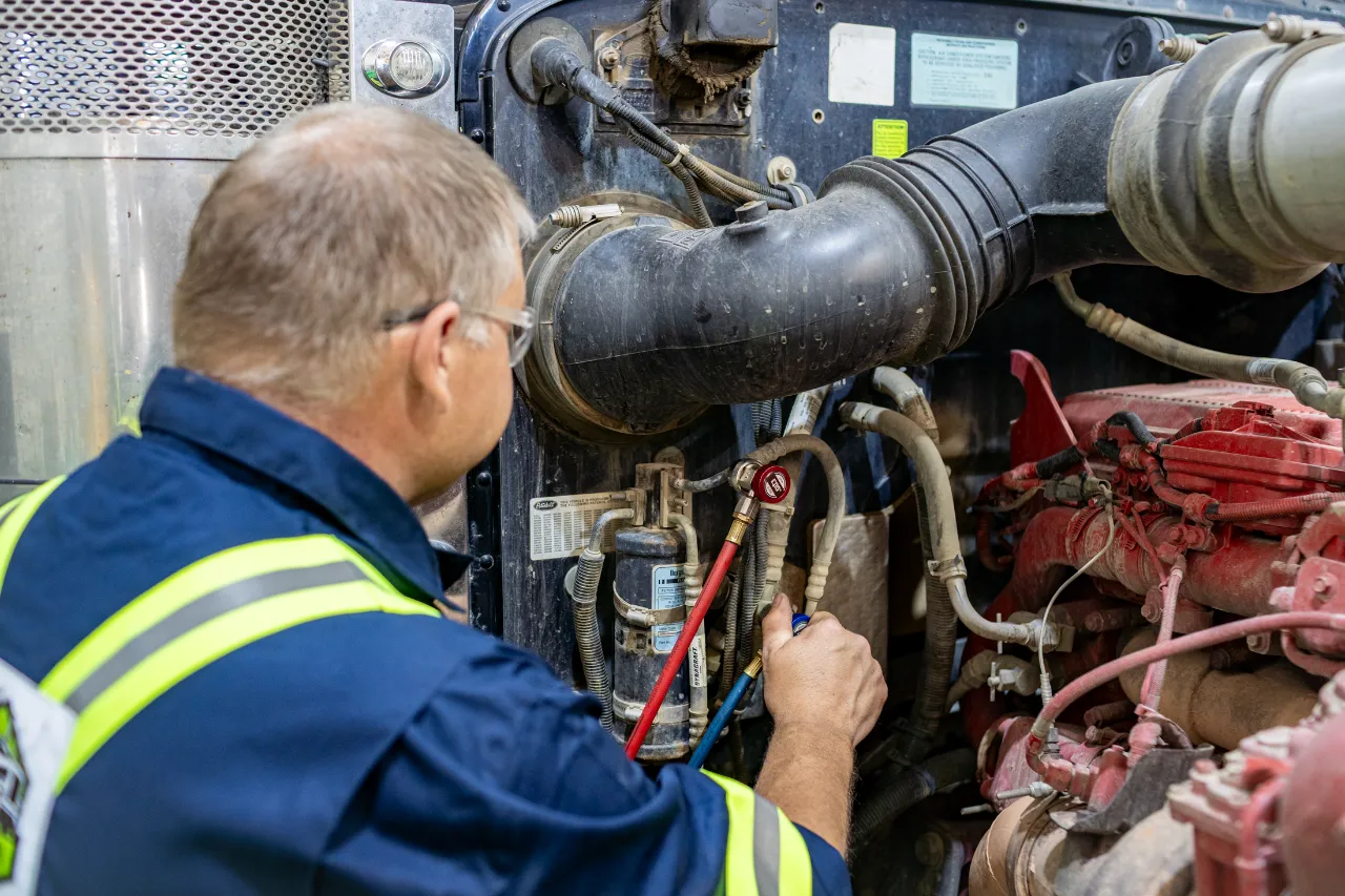 Technician in Edmonton, AB checks fluid levels and hose connections during preventive maintenance on a red diesel engine.