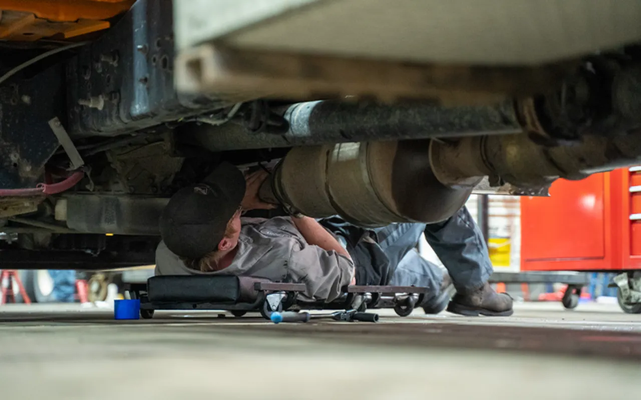 Technician servicing DPF and DEF systems under heavy-duty truck in repair bay.