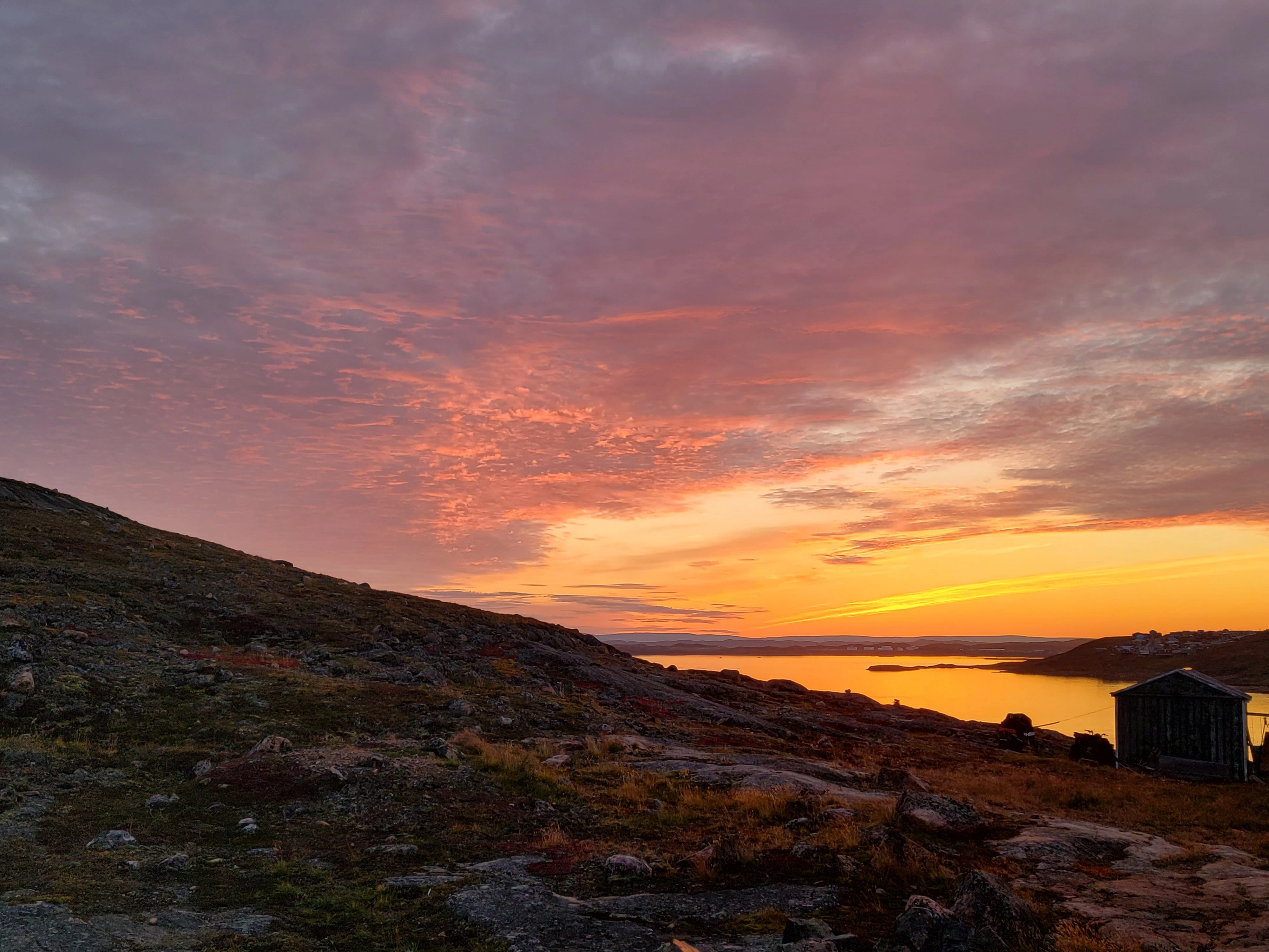 A small house on a hill beside the sea at sunset.