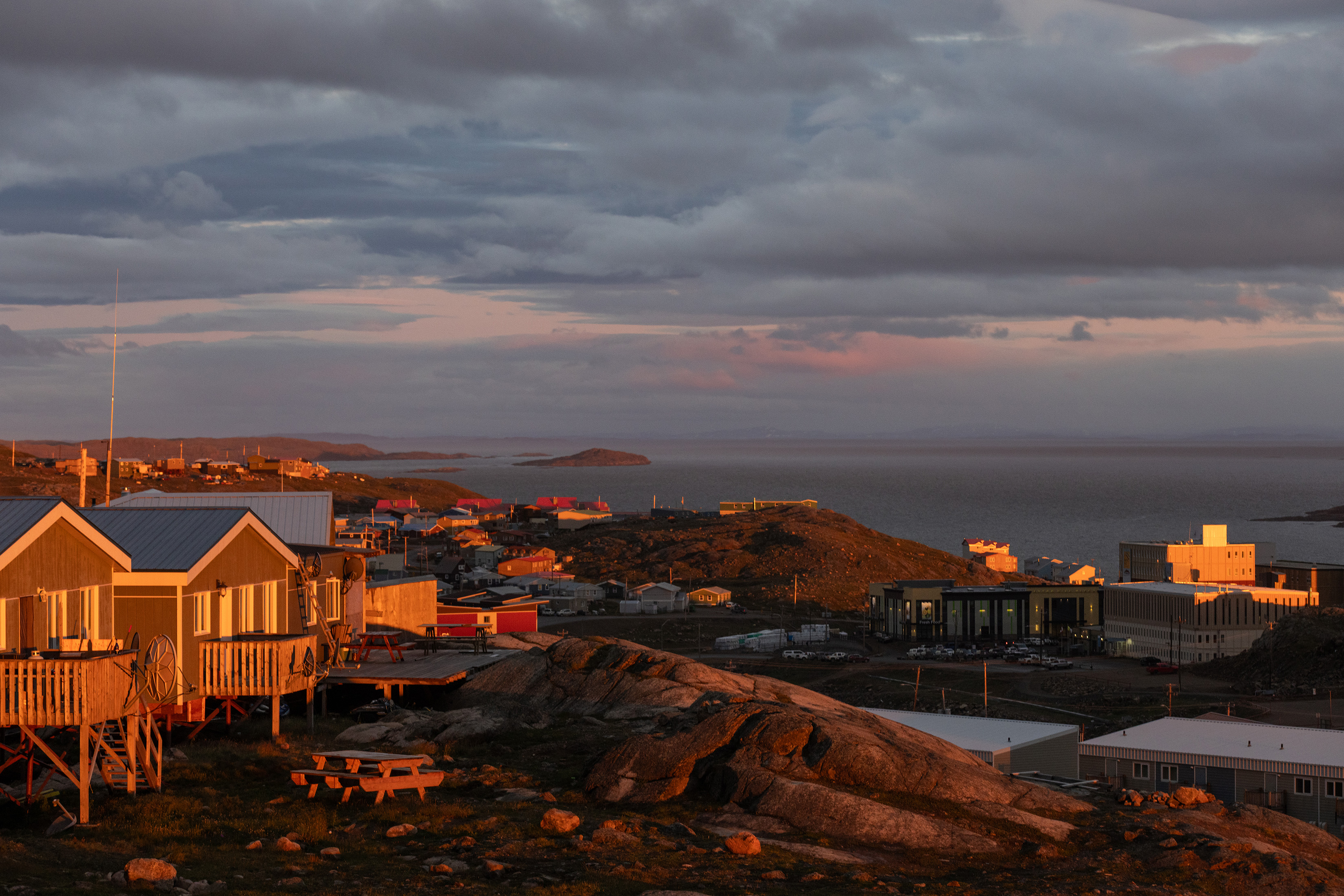 A small house on a hill beside the sea at sunset.