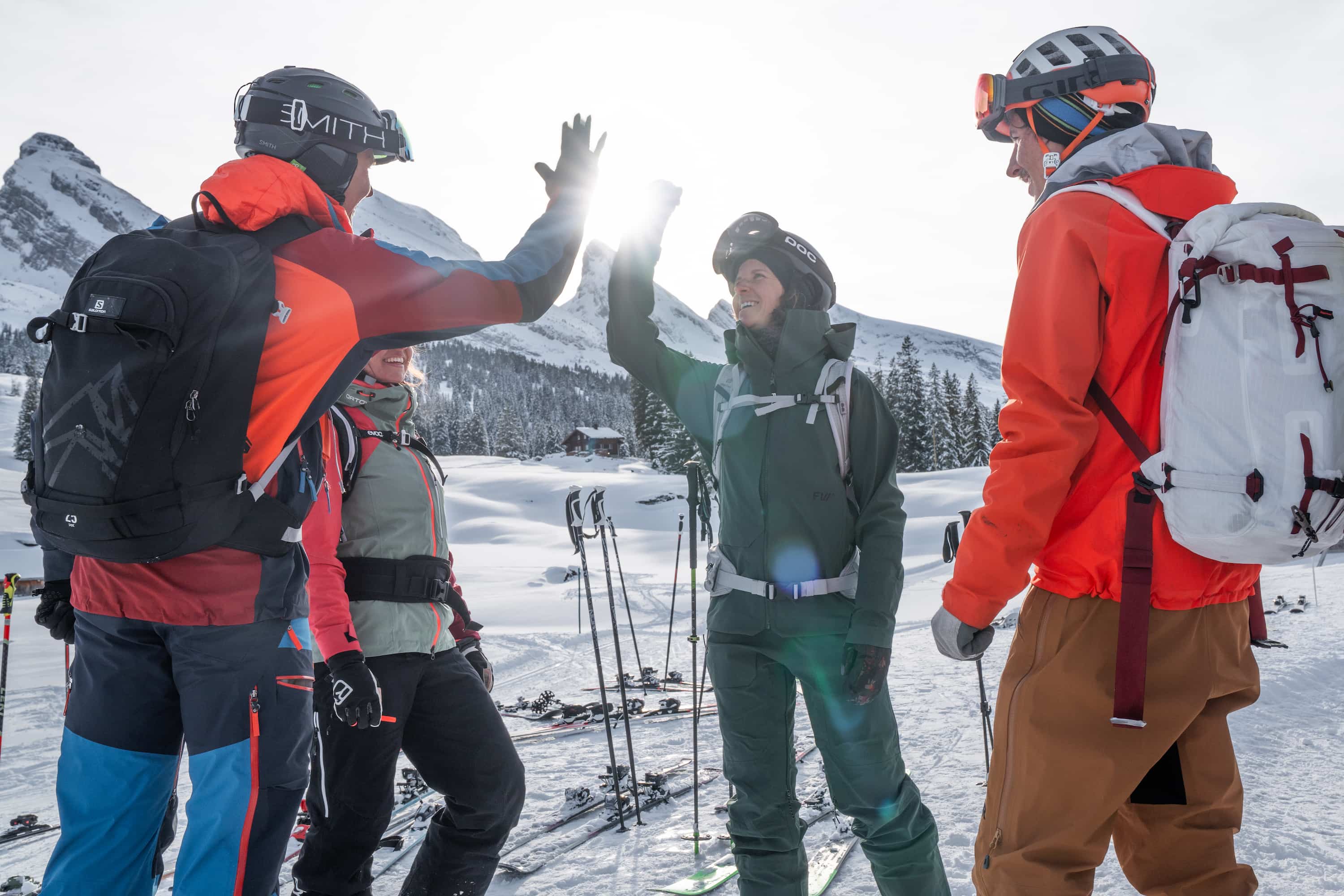 Vier Skifahrer in Winterkleidung und Helmen geben sich vor verschneiter Berglandschaft ein High-Five.