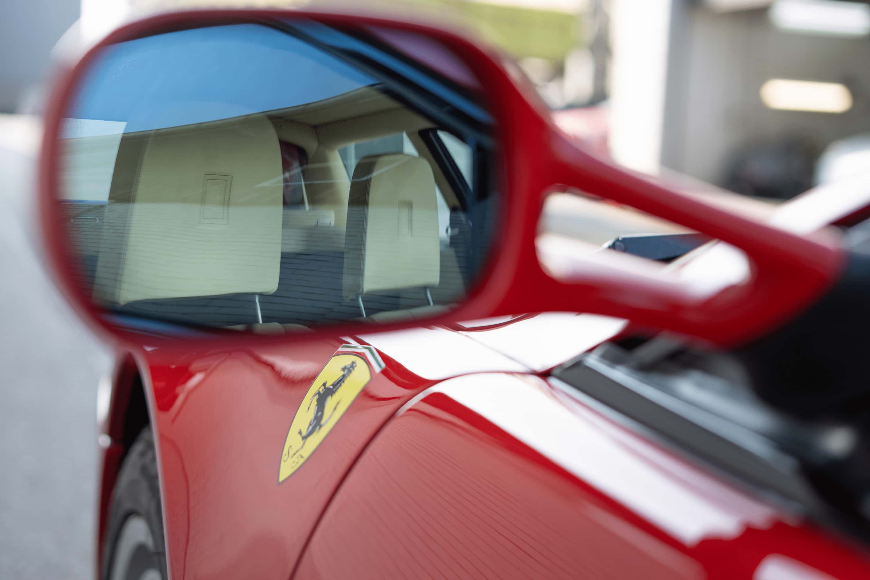 Nahaufnahme eines roten Ferrari mit Fokus auf das Seitenspiegelglas und das Ferrari-Logo am Kotflügel.
