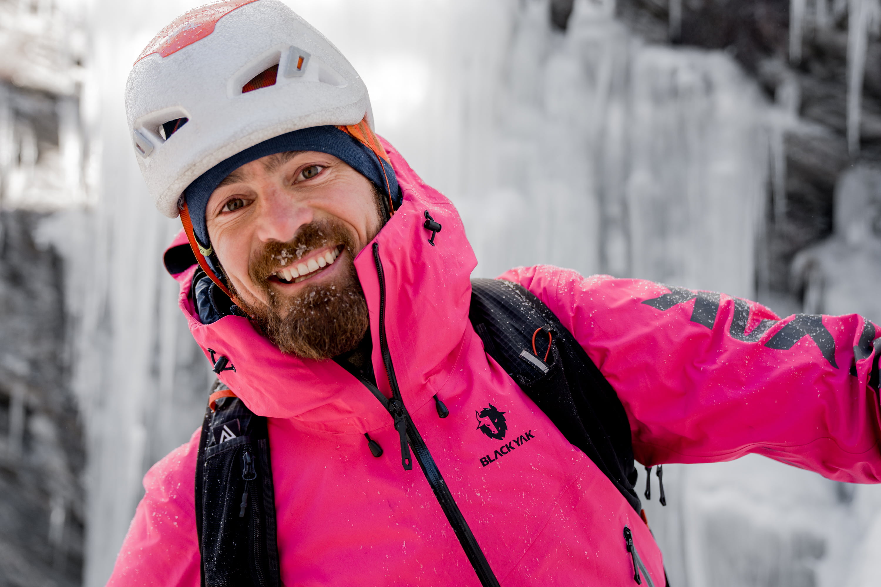 Ein Mann mit Bart und freundlichem Lachen in einem Eisfall mit Helm