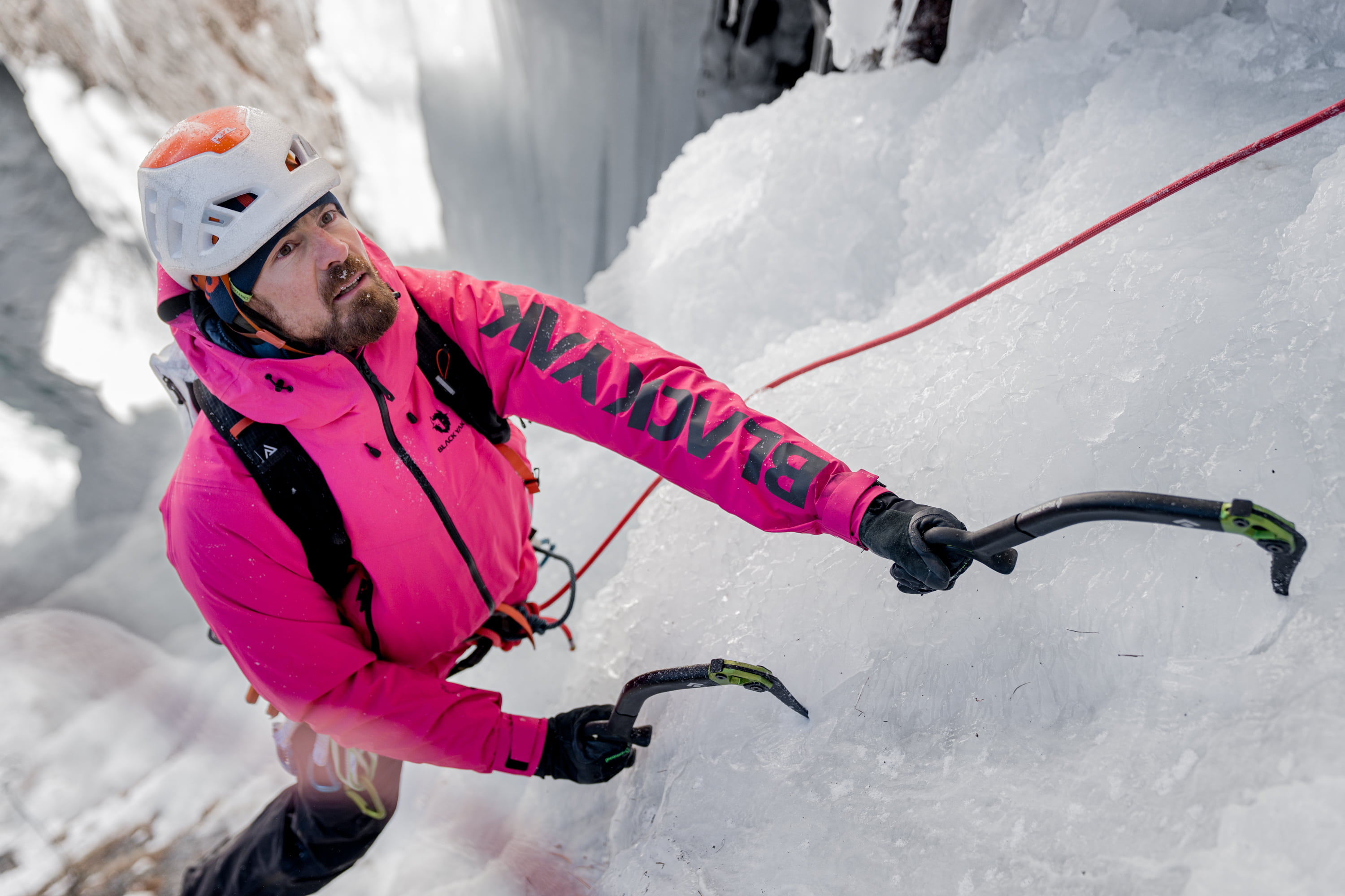 Ein Eiskletterer mit einer Pinken Black Yak Hardshell Jacke schaut nach oben wo es weitergeht