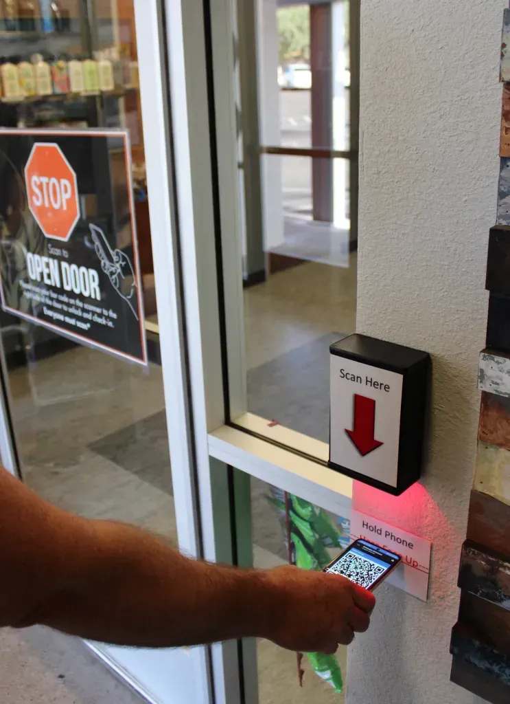 A man is holding a cell phone in front of a red button.