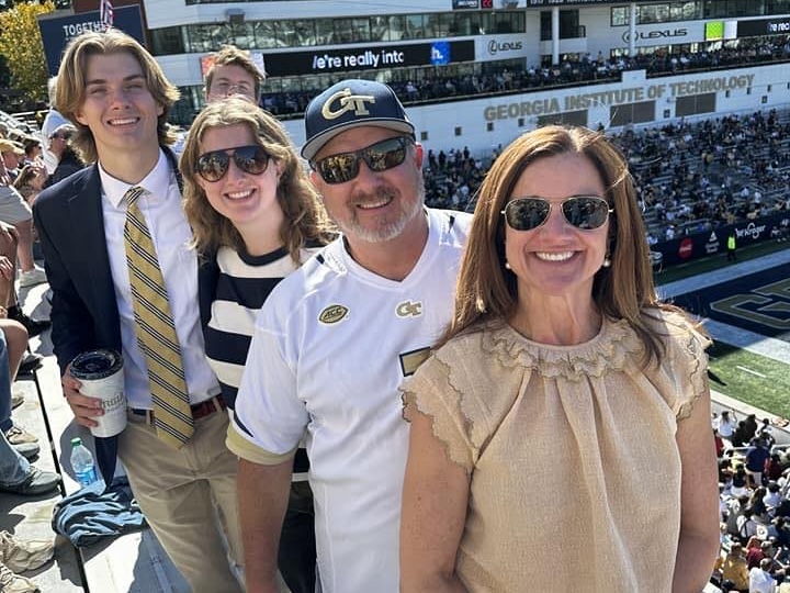Woman, her husband, daughter, and son attend a Georgia Tech game wearing navy and gold.