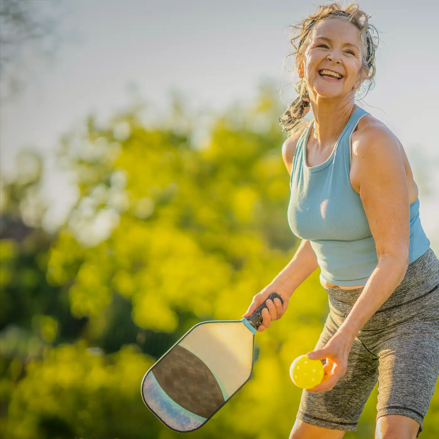 Smiling woman holding a paddle and ball while playing pickleball outdoors