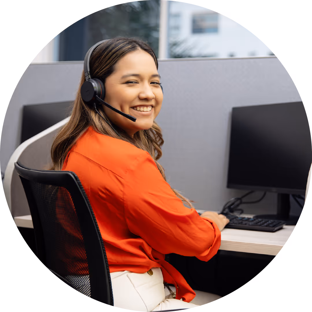 Smiling woman wearing a headset working at a computer in a modern office cubicle.