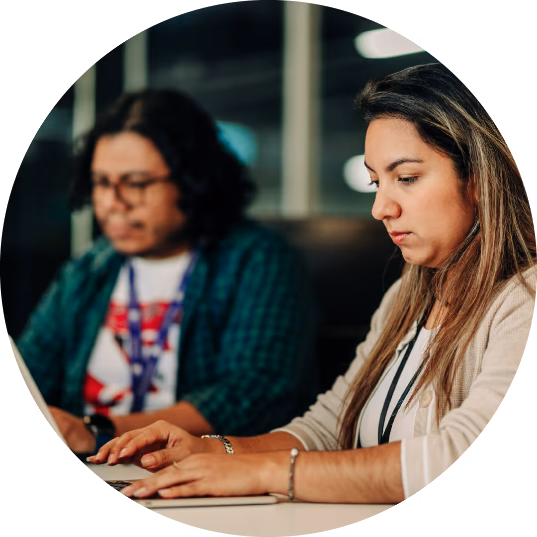 Two people working on laptops in an office environment, focused on their tasks.