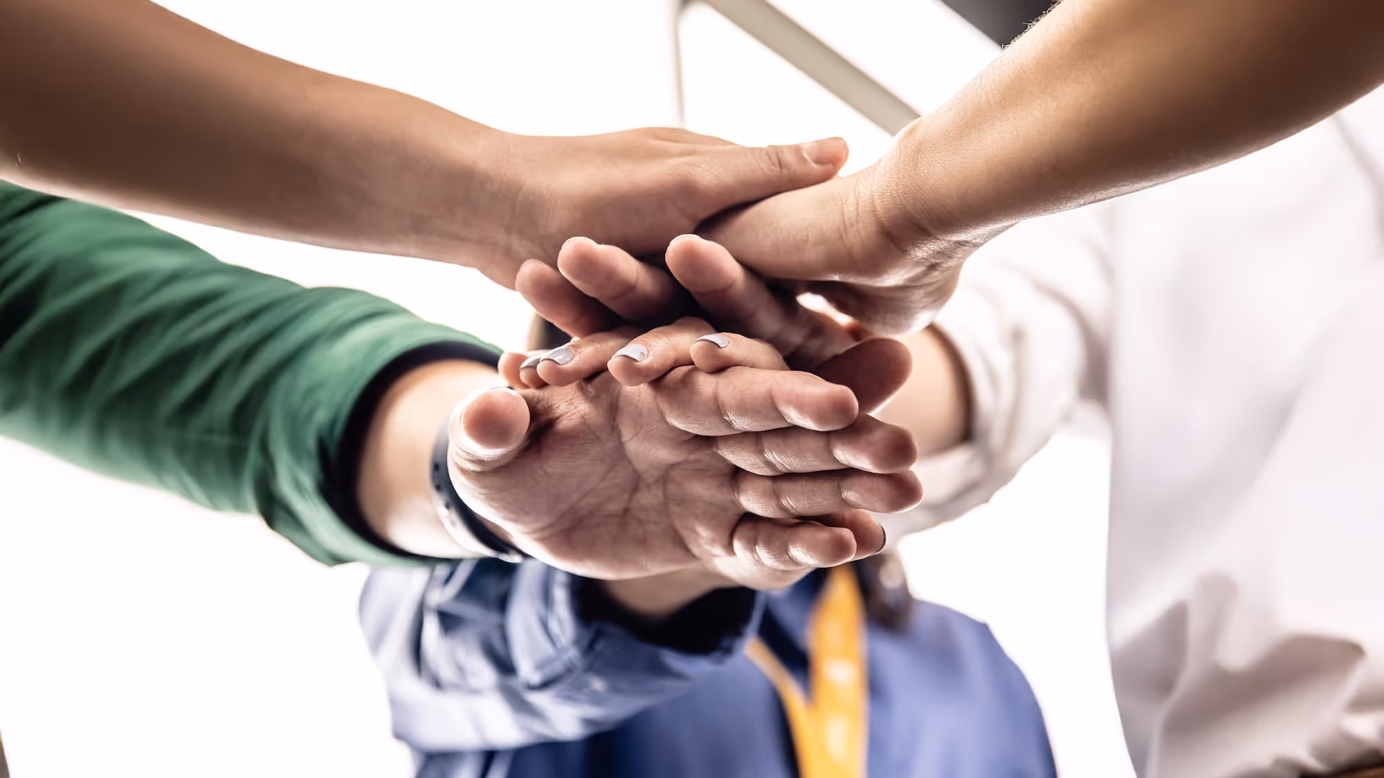 Four people's hands stacked together in a gesture of teamwork and unity.
