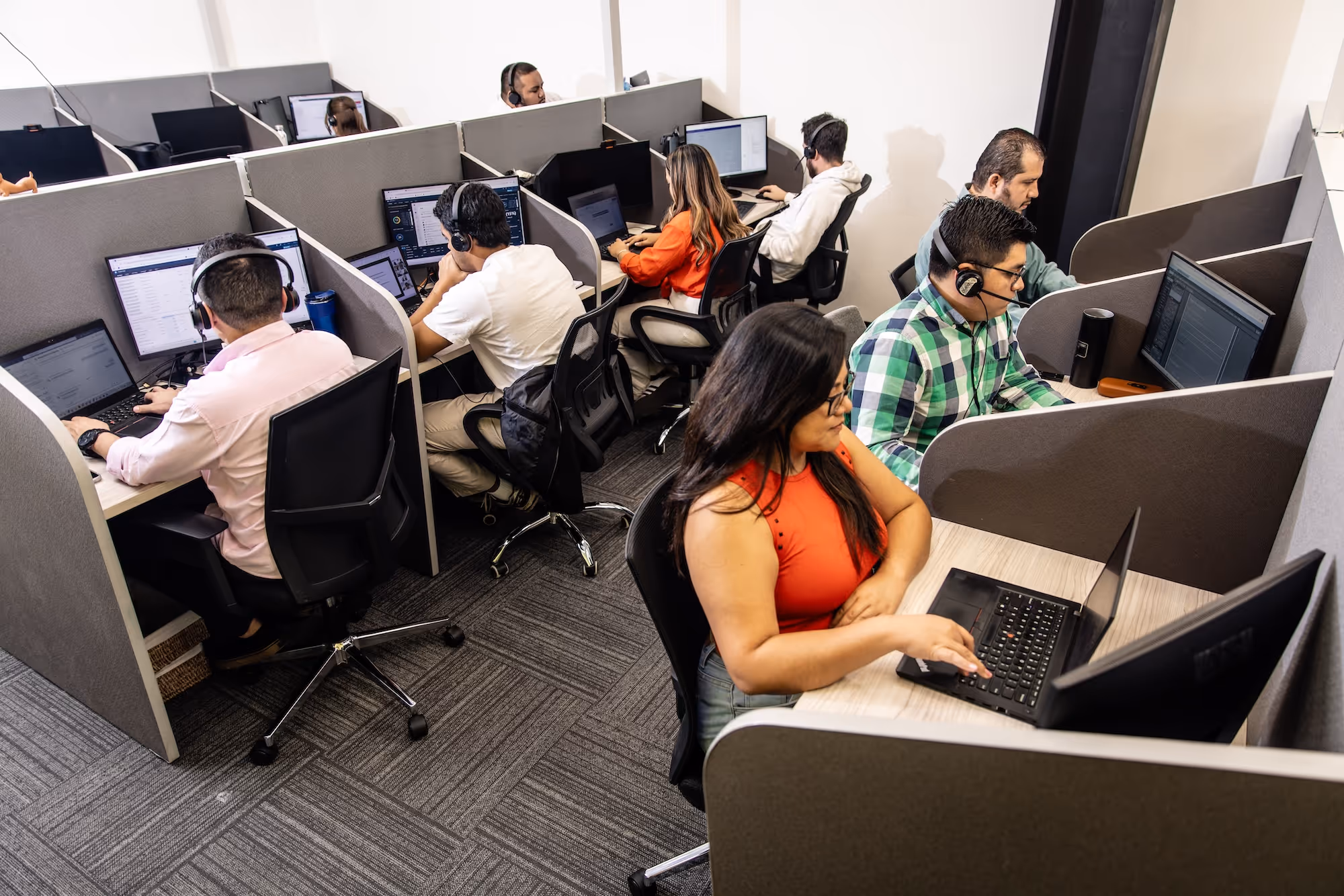 Call center with several people working in cubicles, wearing headsets and using computers.