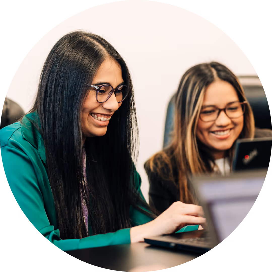 Two women with glasses smiling while working on a laptop together.