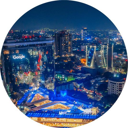 Night aerial view of the El Salvador cityscape featuring the illuminated Presidente Plaza building with surrounding urban structures and roads.