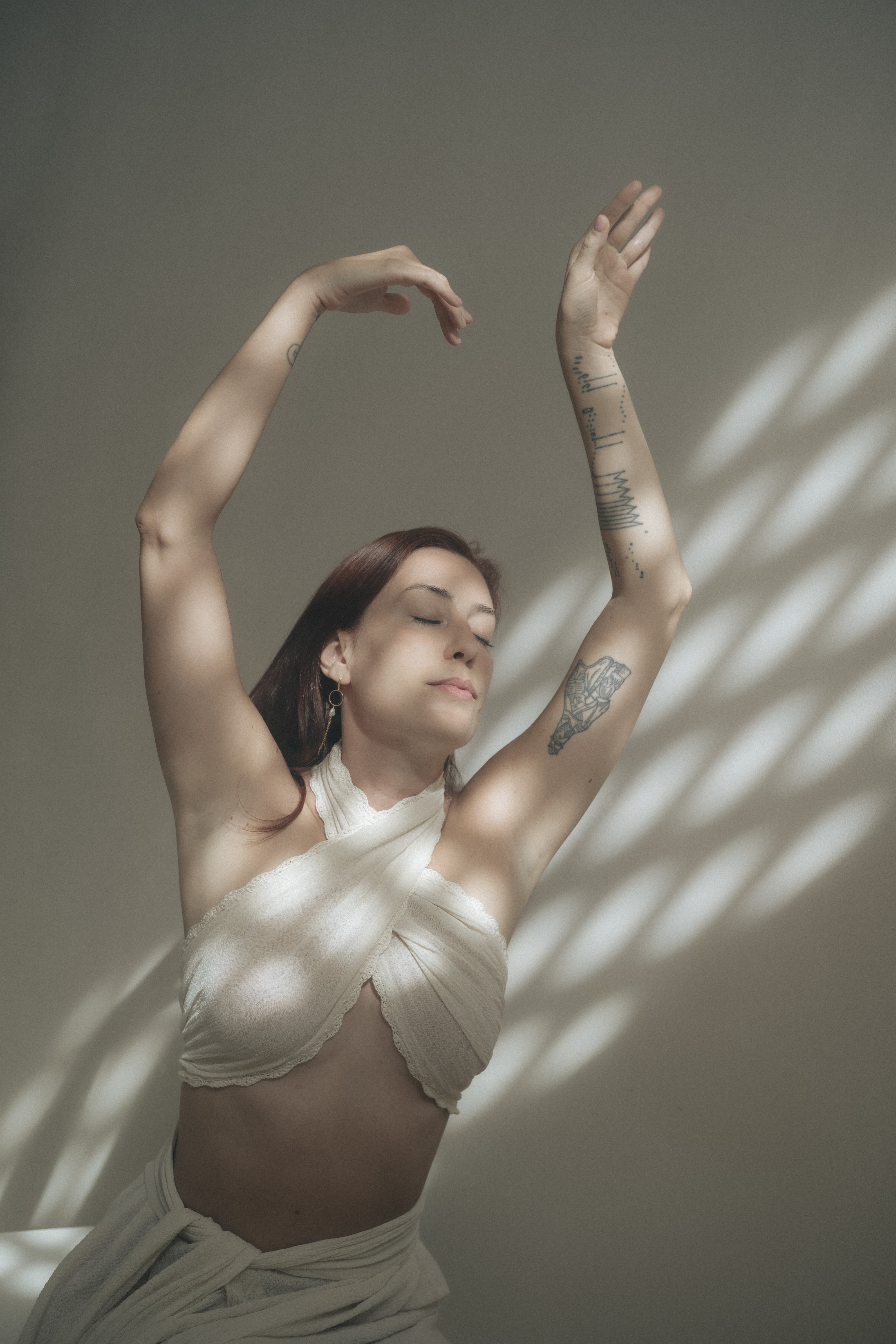 Delfina moving with her arms raised in soft patterned light