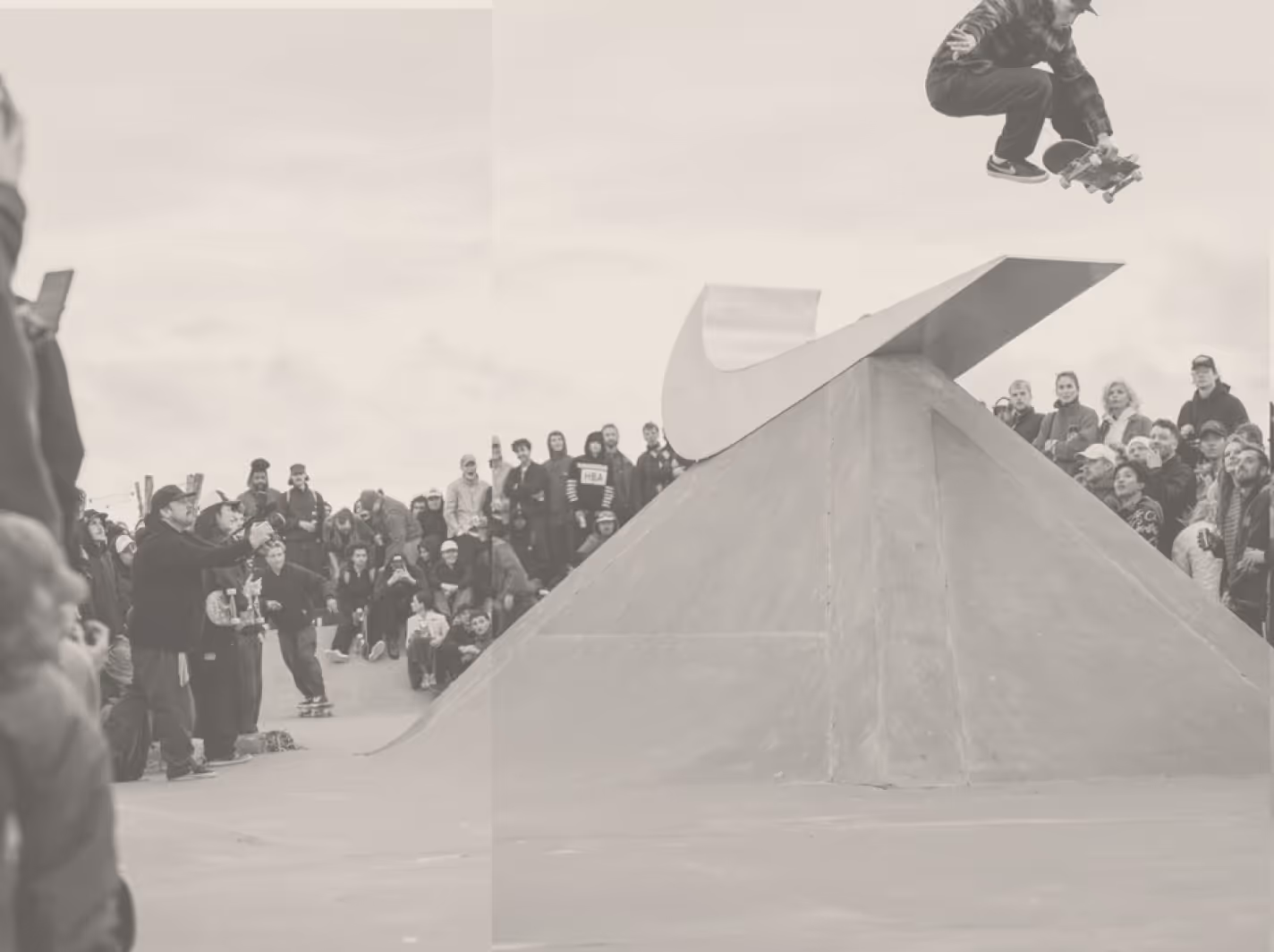 A crowd of people at a skatepark gathered around a skater at a Nike SB event. The skater is suspended in air. 