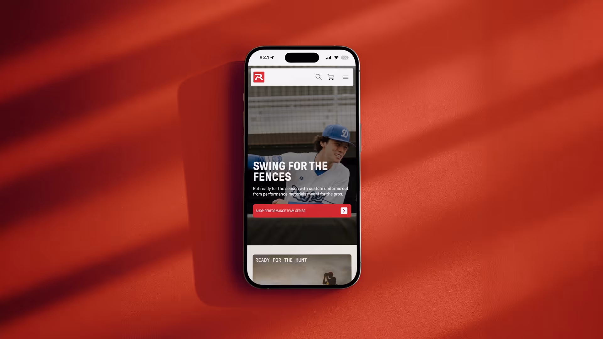Smartphone on red surface displaying a sports apparel website with 'Swing for the Fences' banner and baseball player.