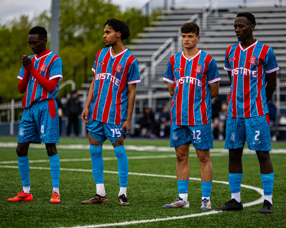 Four soccer players standing on a field wearing blue and red striped Upstate jerseys with numbers 4, 79, 12, and 2.