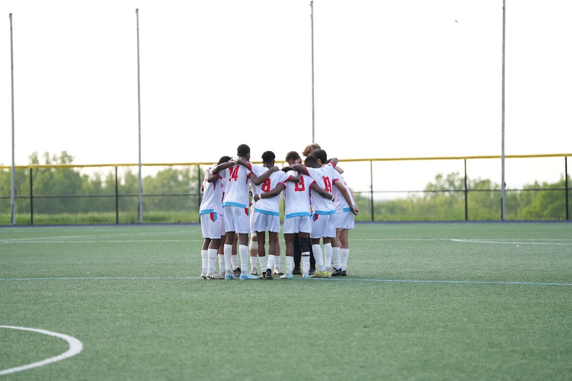 Youth soccer team in white uniforms huddled together on a green field.