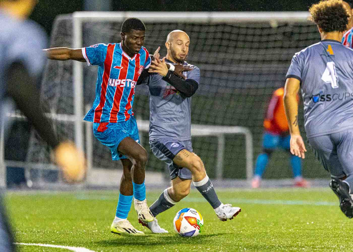 Two soccer players competing for the ball near the goalpost during a night match.