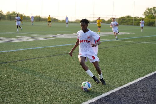 Soccer player wearing white Upstate jersey with number 8 controls a colorful soccer ball near the field sideline during a match.