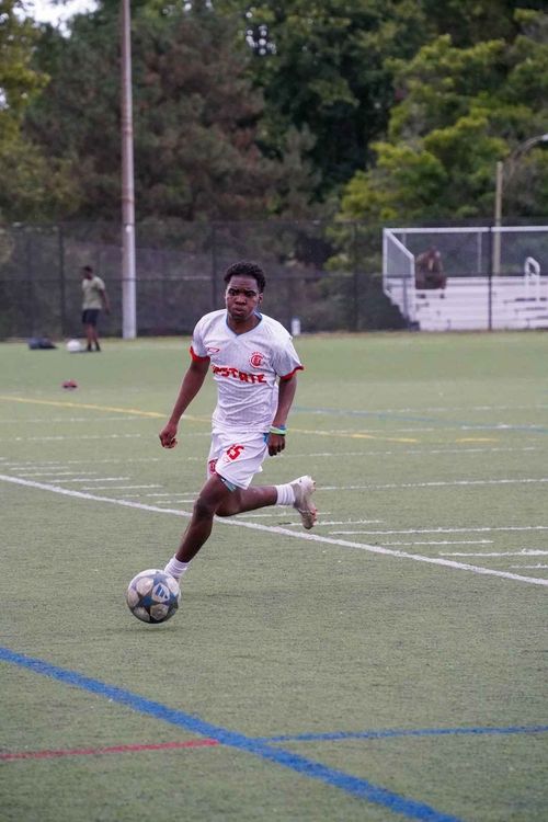 Soccer player in white and red uniform running on the field while controlling a soccer ball.