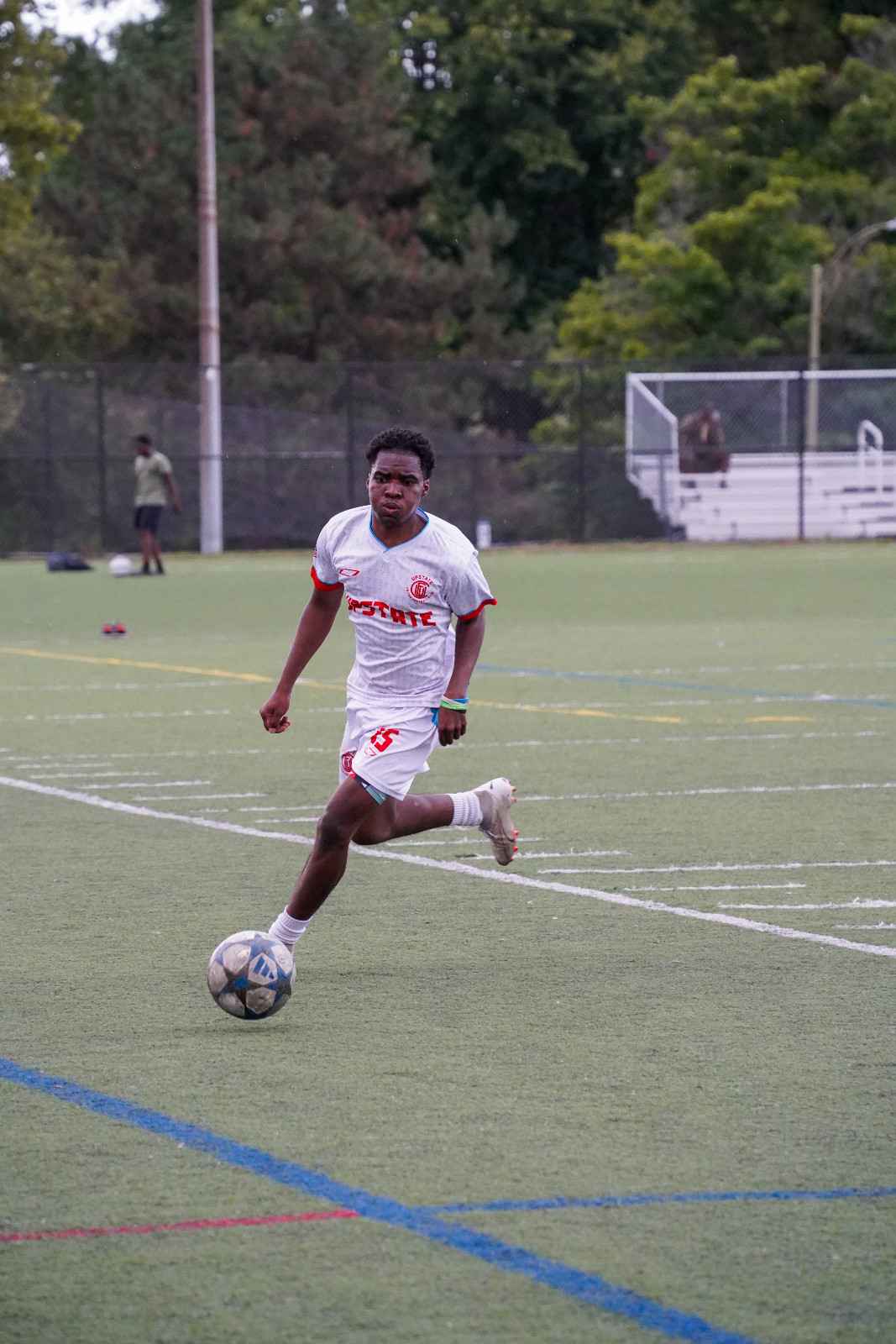Soccer player in white and red uniform running on the field while controlling a soccer ball.
