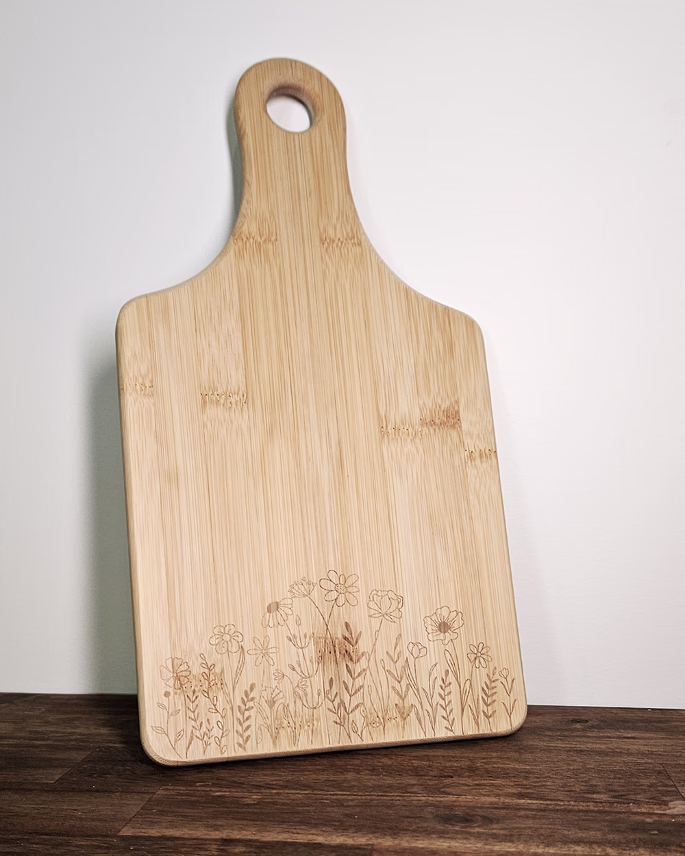 A bamboo cutting board with engraved flowers on the bottom.