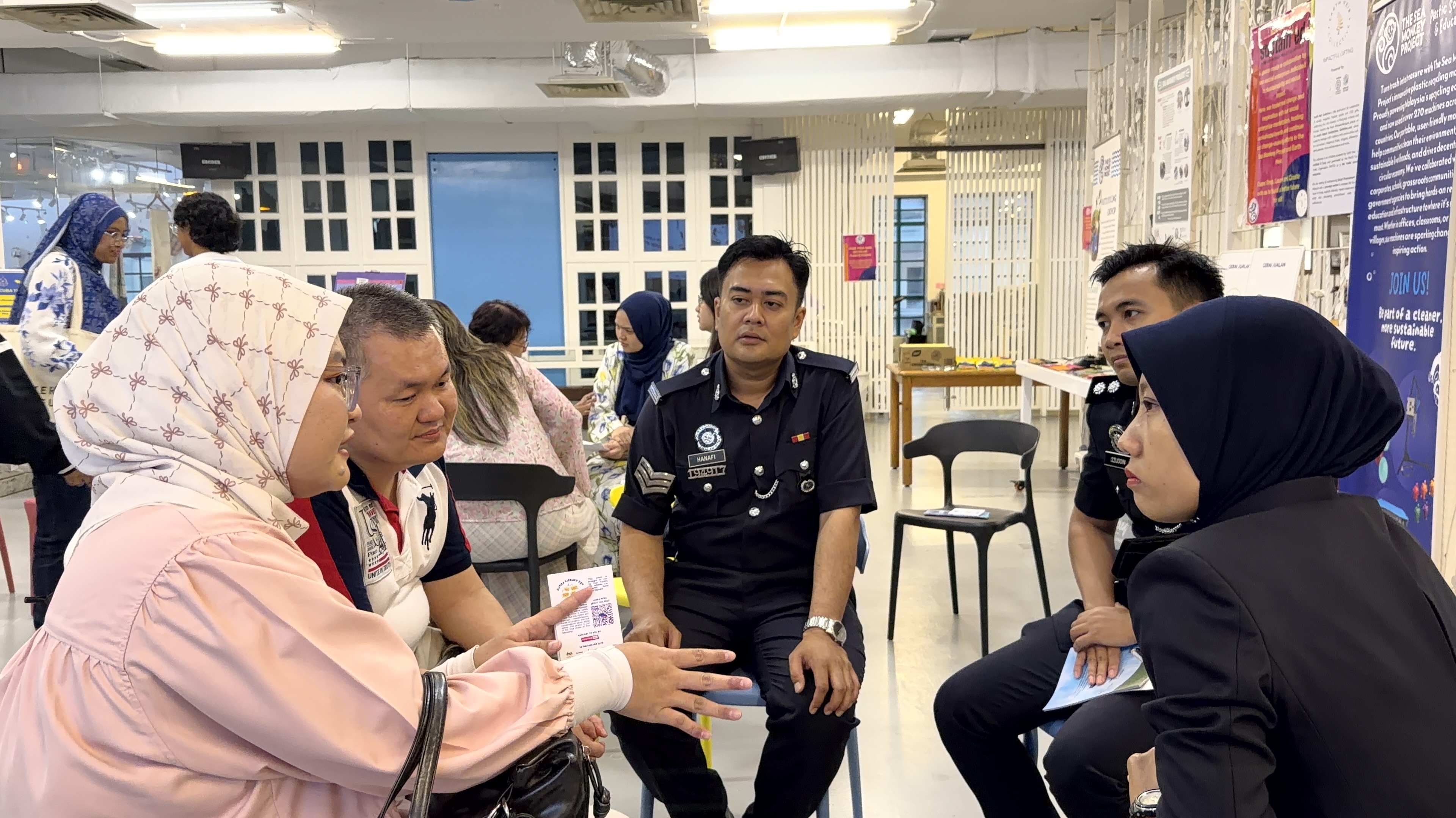 Group of people including two men in police uniforms and others in conversation in a room with posters.