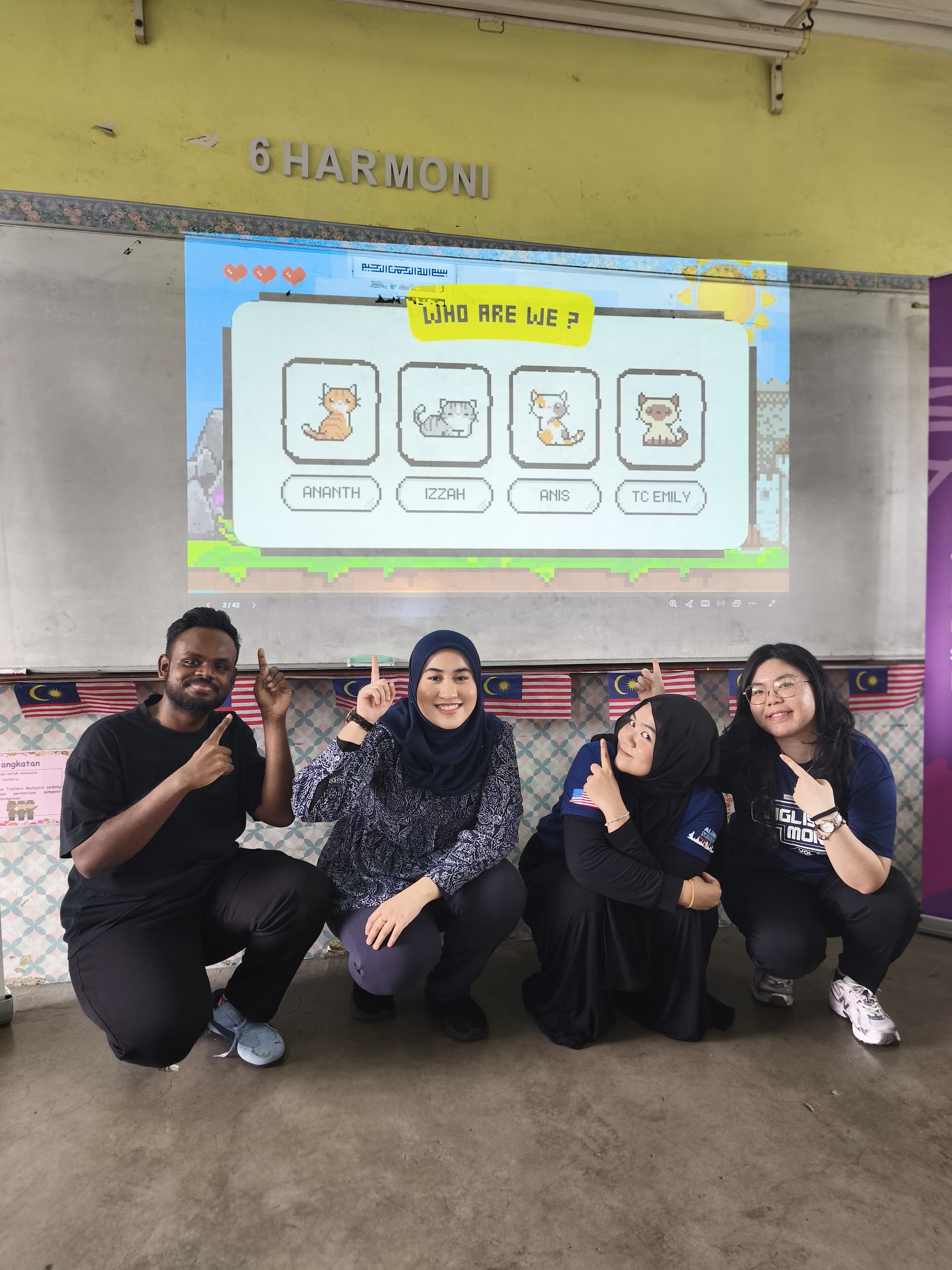 Four people smiling and pointing up at a screen showing cartoon cats with names in a classroom.