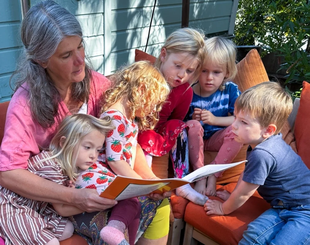 Teresa reading a storybook to a small group of children gathered closely, showing warm family-like care.
