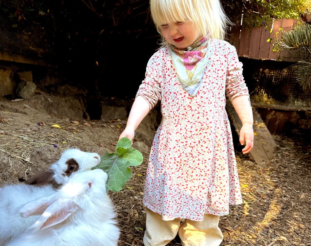 Two children smiling while petting a fluffy rabbit outdoors, highlighting hands-on learning with animals.
