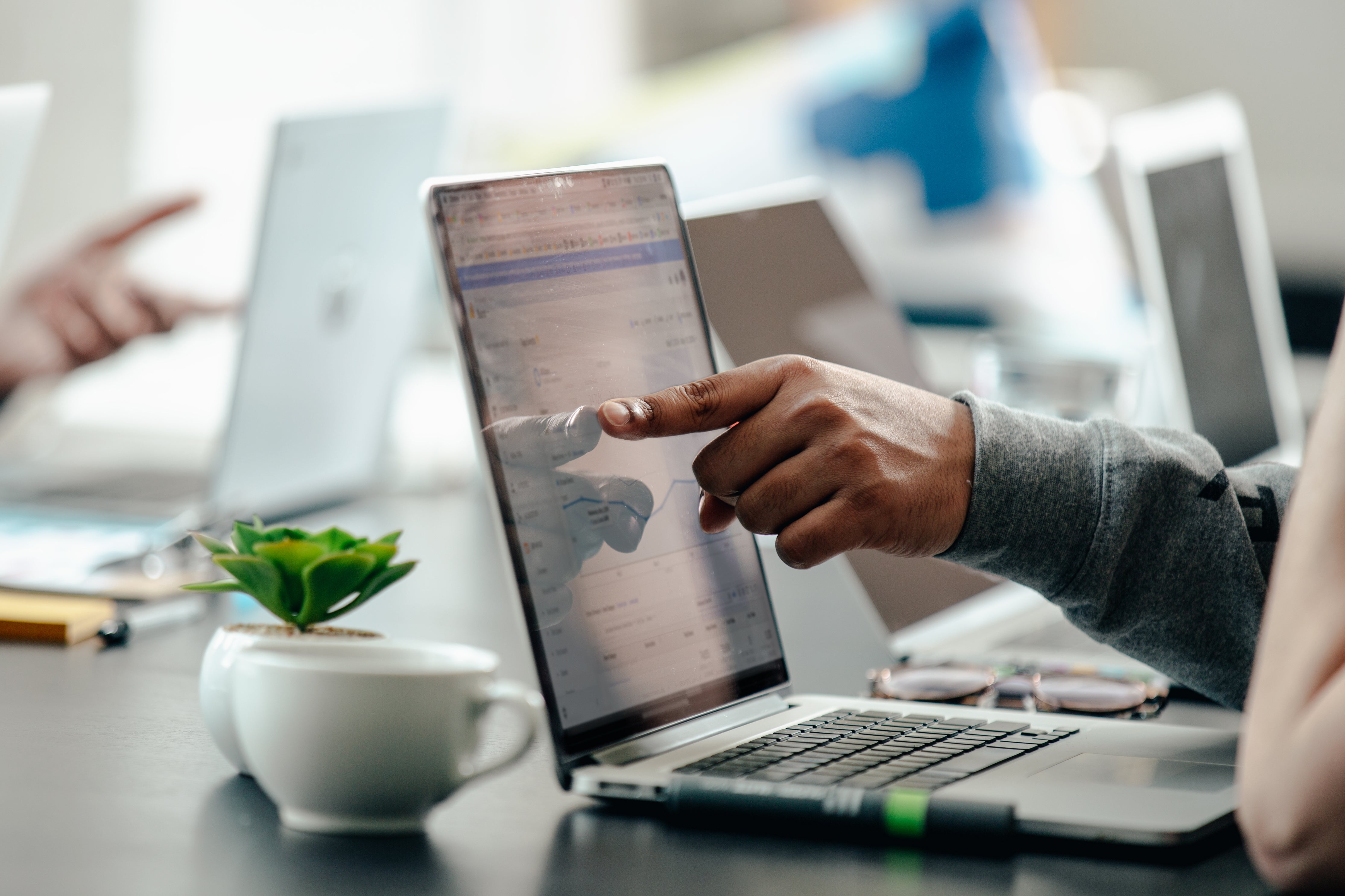 Person pointing at laptop screen displaying data in office setting.