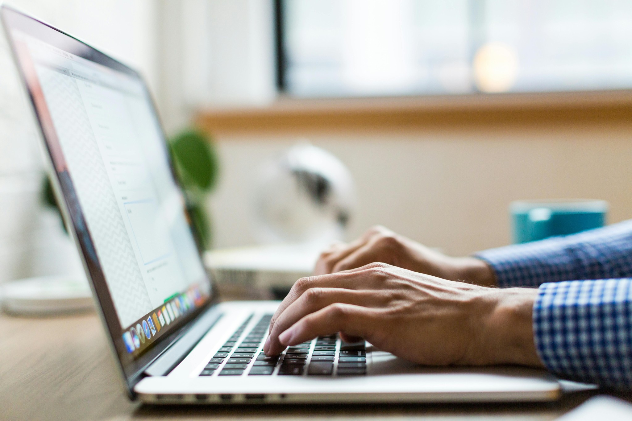 Person typing on laptop at desk near window and mug.