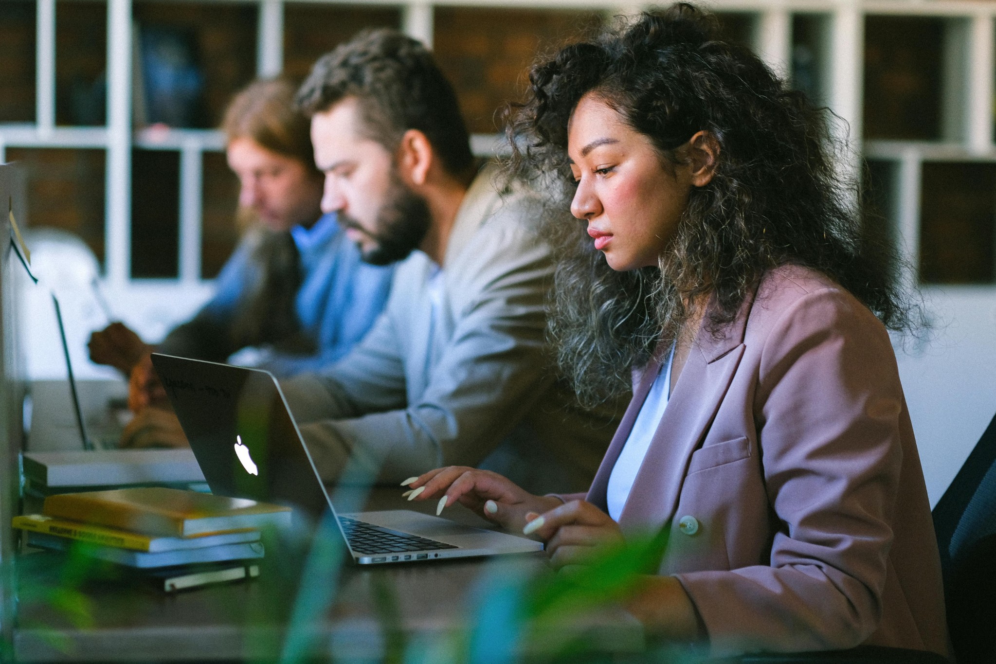 Focused professionals working on laptops at shared modern office desk.