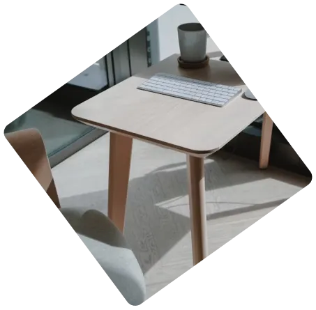 Minimalist wooden desk with a wireless keyboard and a coffee cup in a sunlit room.