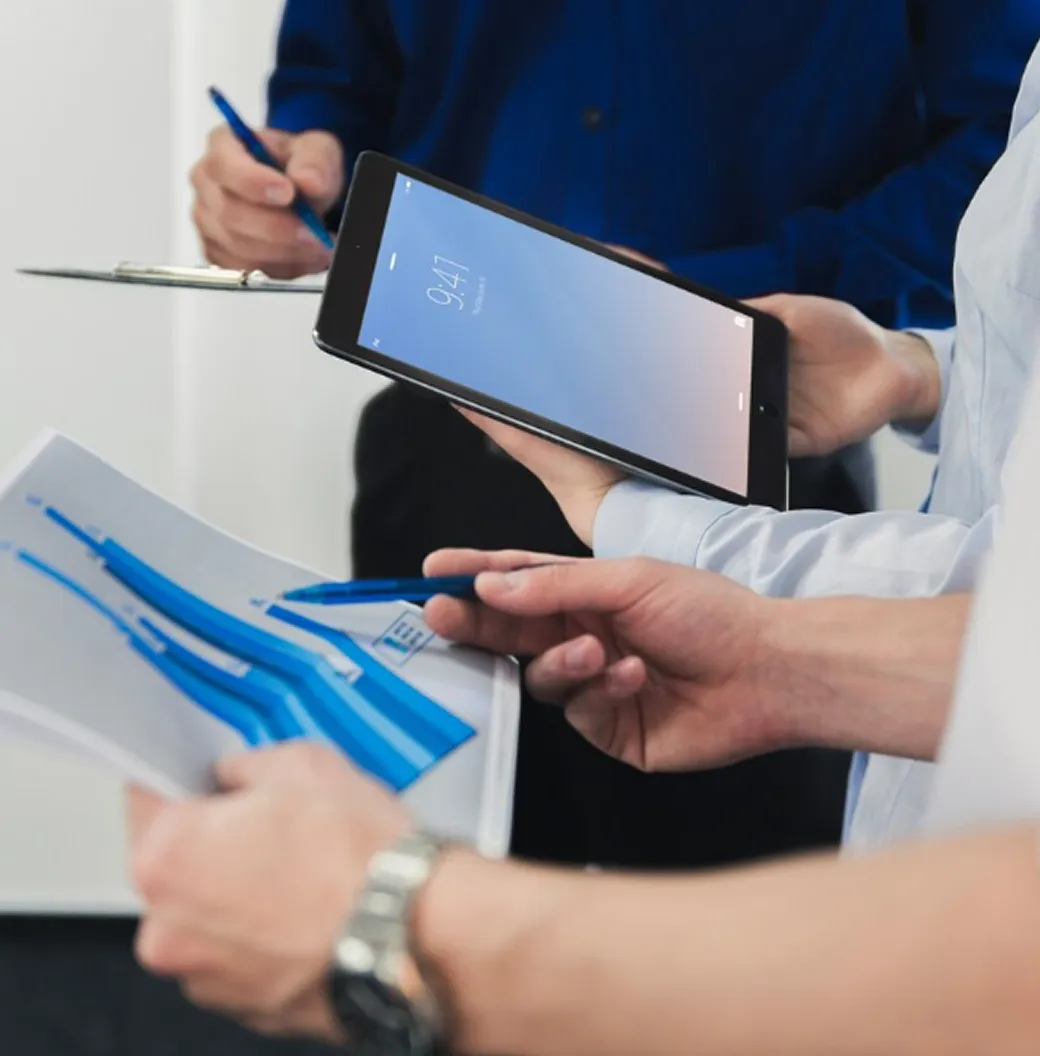 Close-up of people analyzing blue bar charts on paper and a tablet during a business meeting.