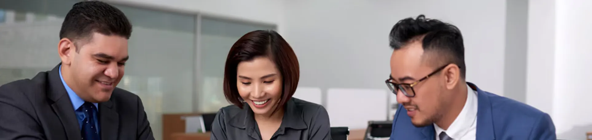 Three business professionals smiling and collaborating in an office setting.