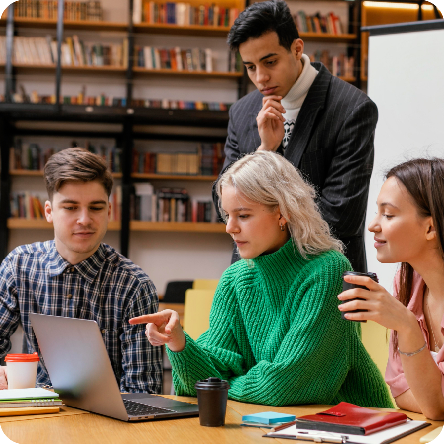 Four young adults collaborating on a laptop in a library.