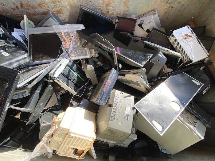 A mound of electronic waste consisting of old computers, broken computer monitors and TVs.