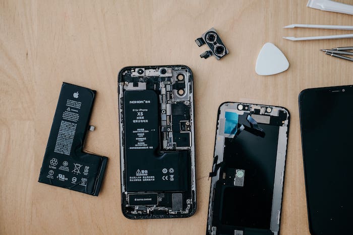An open phone with visible components is being repaired on a light wood table.