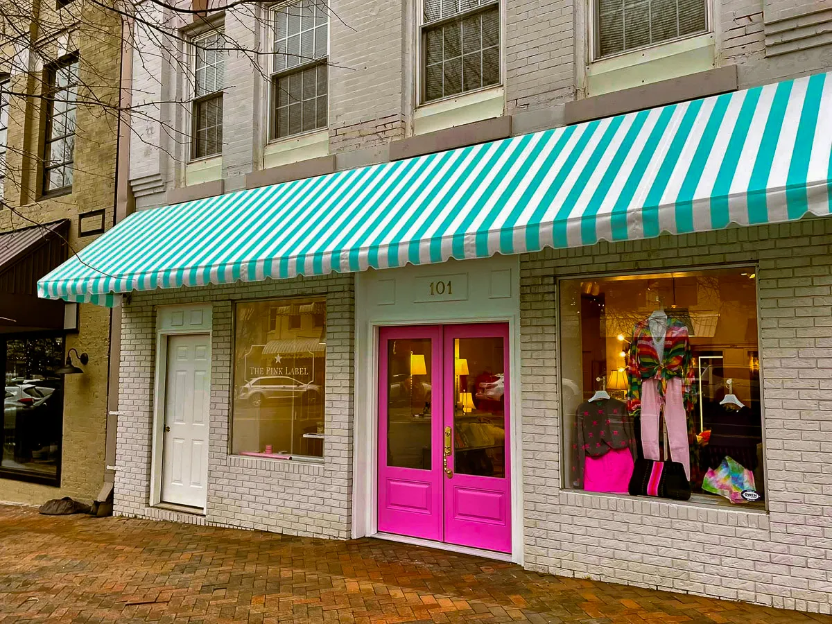 Commercial storefront with teal awnings, pink door, and exterior clothing display signs