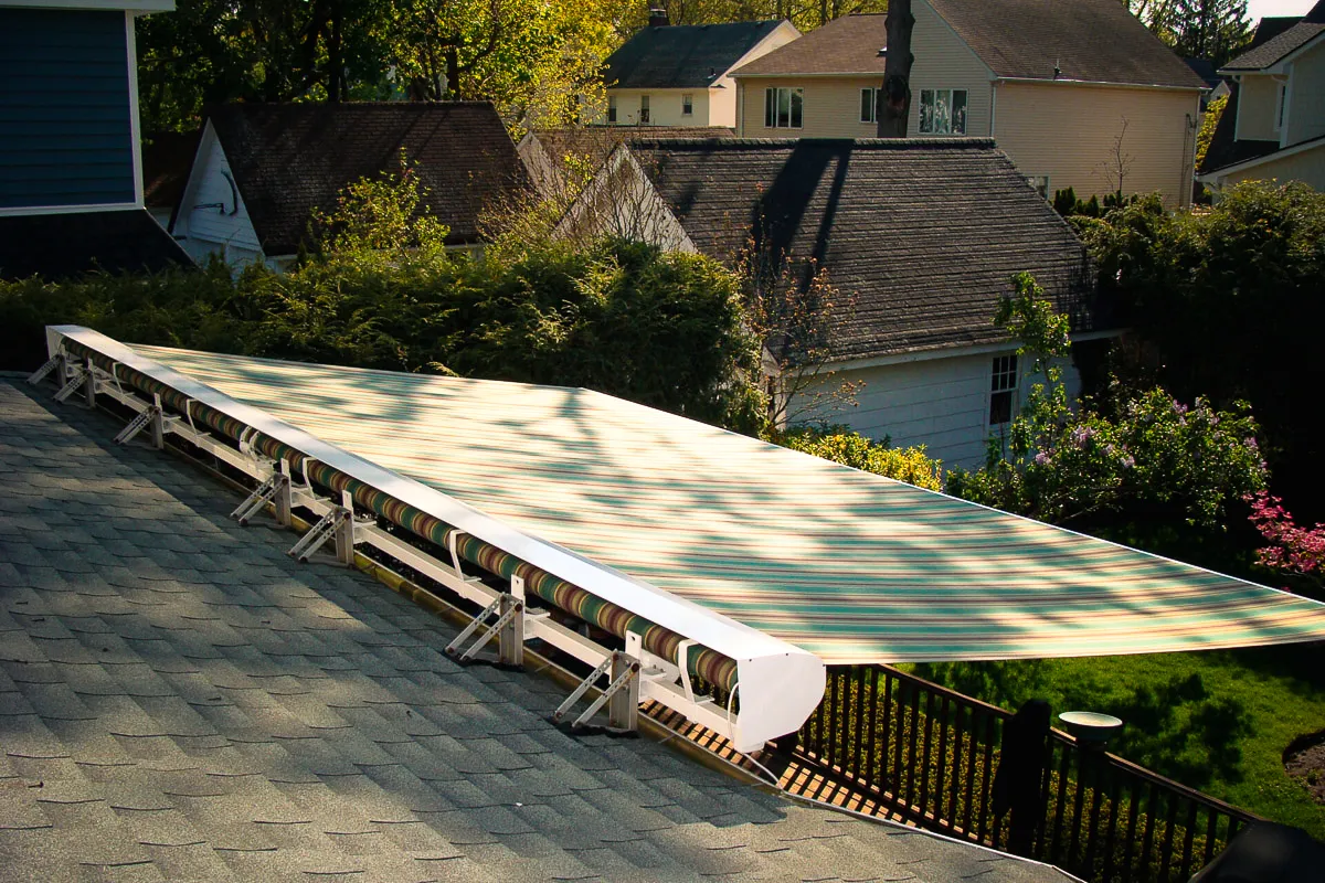 Commercial exterior shade awning mounted on residential roof with neighborhood backdrop
