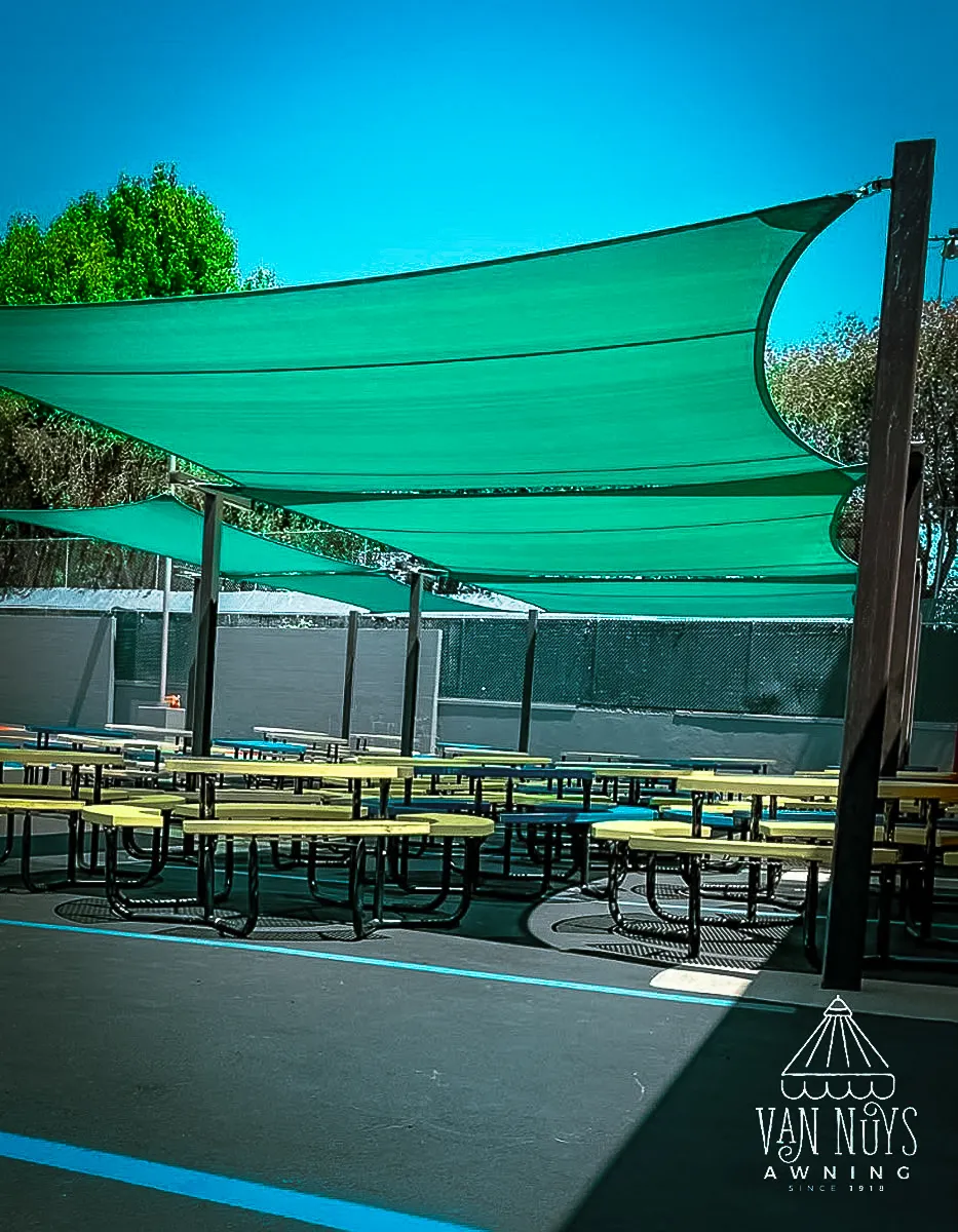 Commercial exterior with green shade sails and yellow tables under awnings