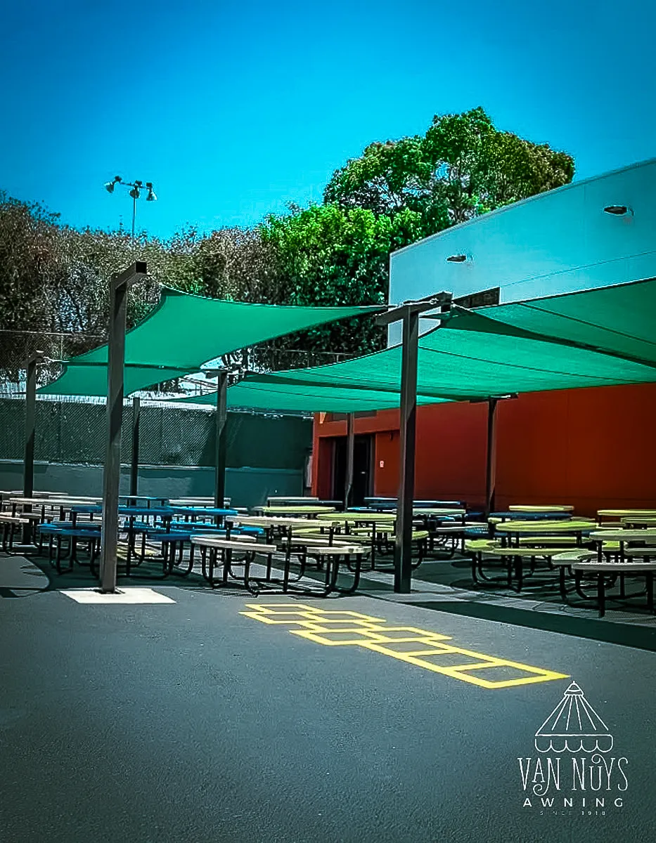 Commercial exterior with green shade sails, picnic tables, and building signs