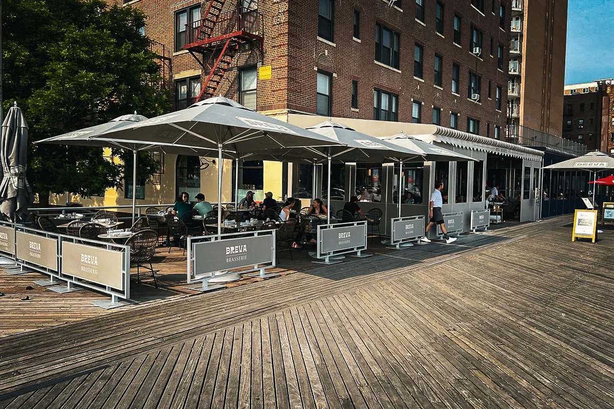 Commercial exterior Breva Brasserie with shades, signs, and outdoor seating