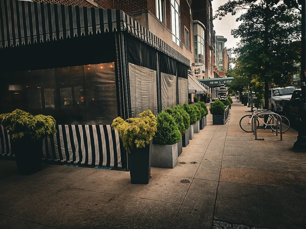 Commercial exterior with awnings, shades, and potted plants on urban sidewalk