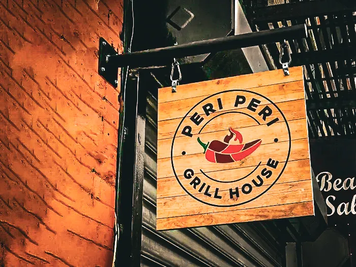 Commercial exterior wooden sign for Peri Peri Grill House with chili logo
